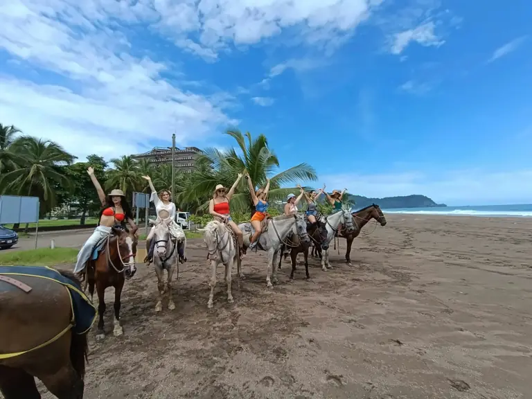 Grupo a caballo en la playa de Jacó, saludando con los brazos en alto