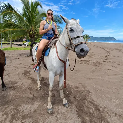 Visitante en un caballo blanco sobre la arena, con palmeras detrás