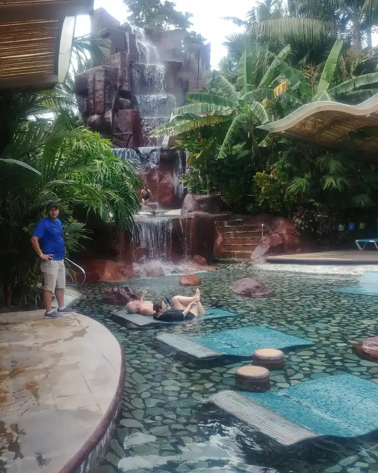 Piscina termal de Spring Paradise con cascada de roca y camastros dentro del agua